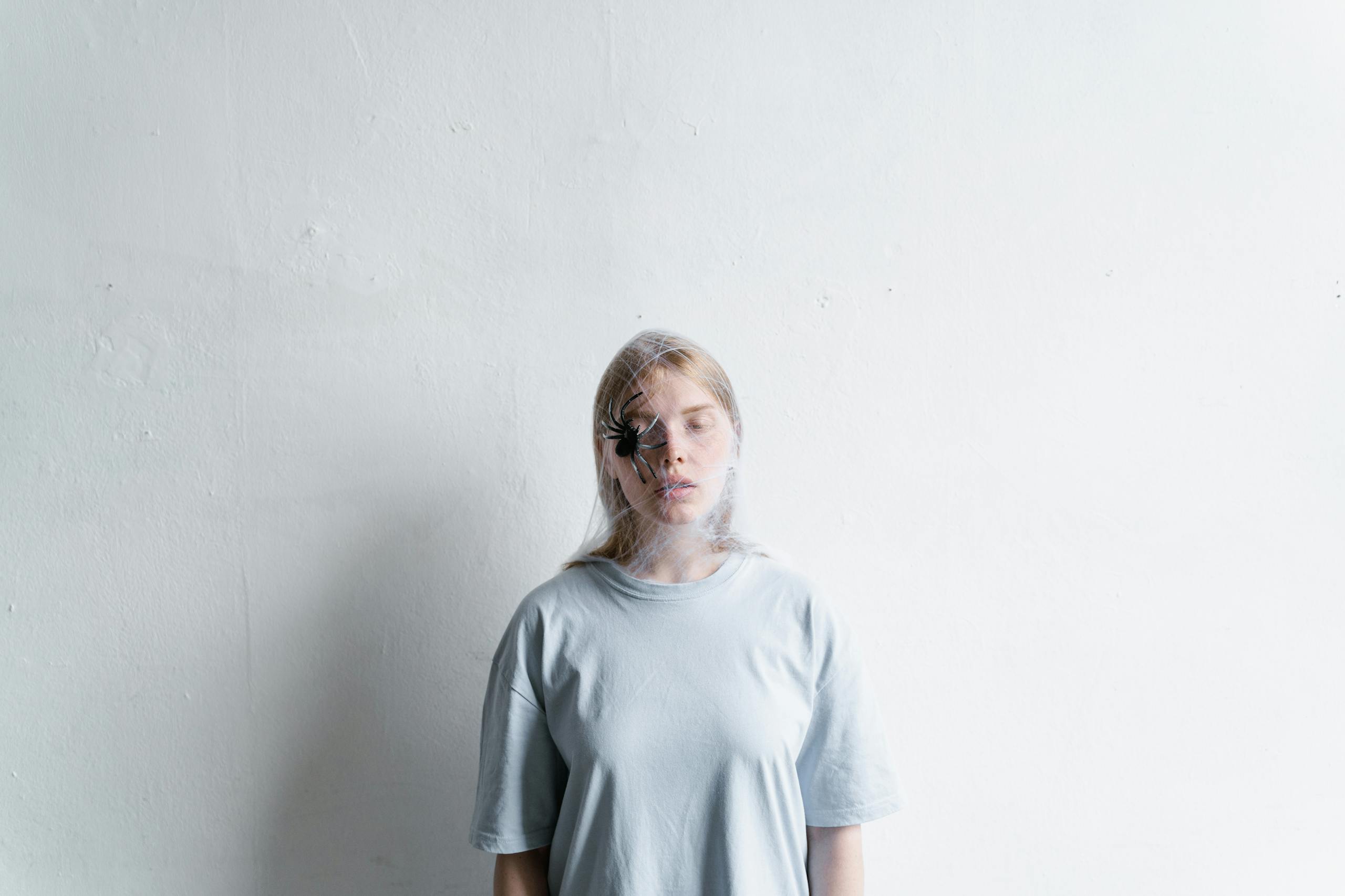 A young woman with a spider on her face symbolizes anxiety and fear against a white background.